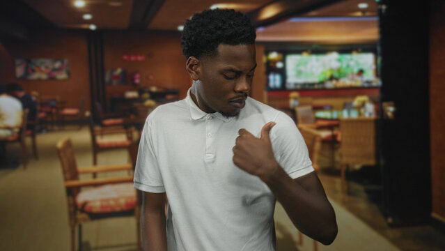 Young african american man adjusts white polo collar in crowded restaurant bar; quiet confidence.