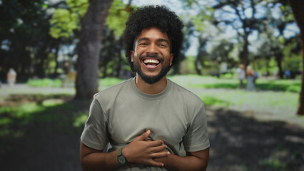Fototapeta premium Man laughing in a green park with trees and sunlight creating a cheerful outdoor ambiance capturing joyful expression and natural setting.