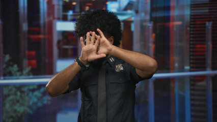 Man in police uniform inside a hotel making stop gesture with both hands against a blurred indoor...