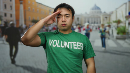 Asian man in green volunteer shirt saluting in st. peter's square, vatican city, with blurred...