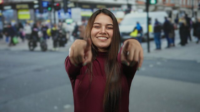 Woman smiling and pointing playfully on a busy city street with blurred pedestrians and vehicles in the background, capturing a vibrant urban outdoor scene. - Powered by Adobe