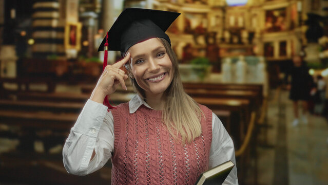 Woman smiling in graduation cap holding book in church setting, signifying academic achievement and contemplation.