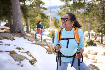 Female hiker enjoying a snowy mountain forest trail, equipped with backpack and trekking poles, embracing the serene winter landscape