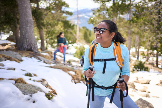 Female hiker enjoying a snowy mountain forest trail, equipped with backpack and trekking poles, embracing the serene winter landscape
