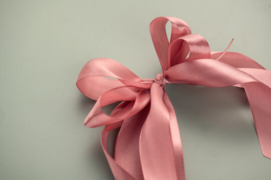 Pink satin gift bow over pastel background. Holiday decoration silk ribbon, top view, border art. Beautiful gift design.