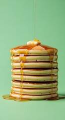 Stack of fluffy pancakes drizzled with golden syrup and topped with a dollop of whipped cream and a small piece of fruit, set against a pastel green background