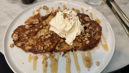 Caramelized breakfast french toast with whipped cream, granola, and honey drizzle on white plate