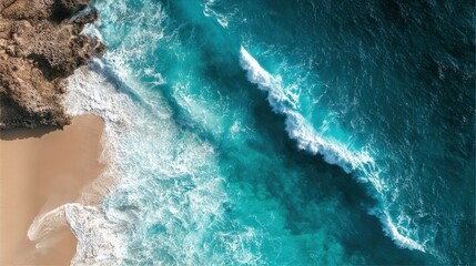 Aerial View of Turquoise Waves Crashing on Sandy Beach Shoreline with Rocky Cliff and Crystal Clear Water Beneath Bright Sunlight