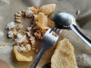 A close-up shot of leftovers from a serving of Nasi Uduk (Indonesian fragrant coconut rice) and crackers (krupuk). The small amount of rice, seasoned with spices and cooked in coconut milk, is scatter