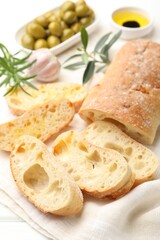 Fresh cut ciabatta, oil, olives and rosemary on white wooden table, closeup