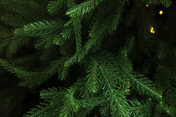 Branches of artificial Christmas tree against bokeh lights, closeup
