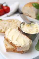 Slices of baguette with butter, basil and knife on white table, closeup