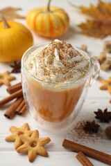 Tasty pumpkin latte with whipped cream in glass cup, cookies and ingredients on white wooden table, closeup