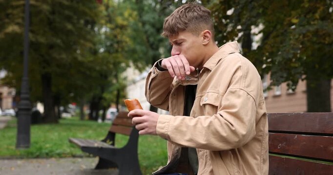 Young man eating bun and suffering from stomachache and nausea outdoors