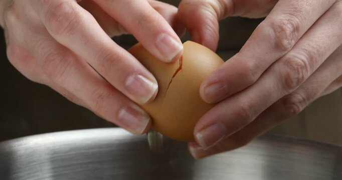 Woman breaking egg into metal bowl, closeup
