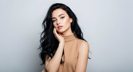 Naklejka premium Beautiful young brunette woman with long wavy hair, hand on cheek, beige turtleneck, soft gray background. Perfect for beauty, fashion, lifestyle ads. 8K, natural, elegant.