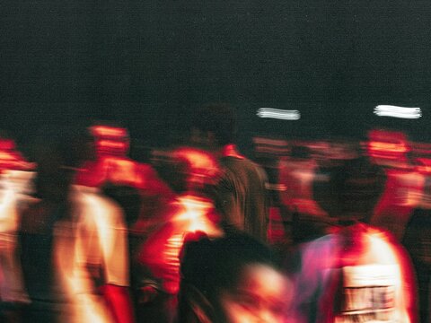 Vibrant lively concert scene, crowd under intense lighting, People move dynamically with flashing device captures Nighttime venue captures motion with vibrant red illumination and obscured faces