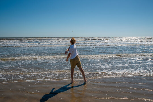 Blond haired boy standing on a beach throwing a stone into the water
