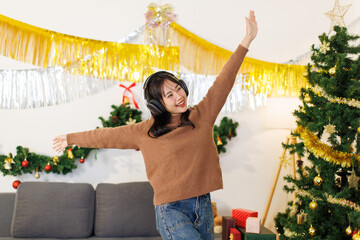 Asian young beautiful woman smile standing listening music with headphones presents box gifts decorated christmas tree in living room, Merry christmas happy new year season holiday festival celebrated