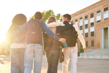 Diverse group of young students embracing while walking outdoors with backpacks after classes