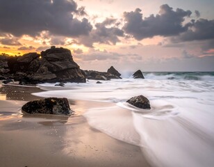 Coastal scene with blurred water and dark rocks under a cloudy sky at sunset