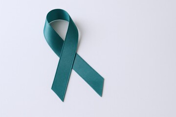 Teal ribbon symbolizing awareness of ovarian, cervical, uterine, and sexual assault, placed on a white surface.