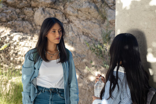 Serious young woman listening intently to her friend during an outdoor discussion, standing next to a rock wall and feeling focused on the conversation