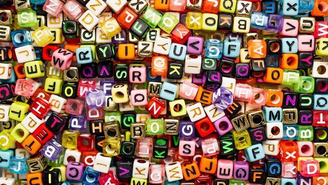 Overhead view of a vibrant, chaotic pile of assorted alphabet letter beads for crafting jewelry.