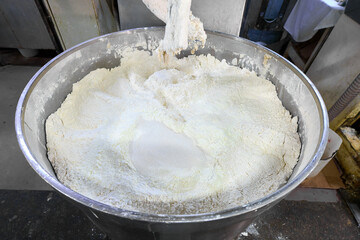 Dough kneading machine mixes flour in a commercial kitchen environment for baking preparations and pastry-making processes