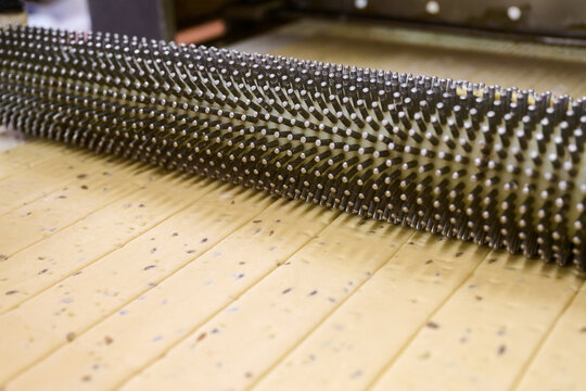 Cracker dough being processed through a docker machine to create uniform perforations before baking