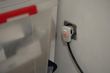 Close-up of a white electrical adapter with a red indicator light plugged into a wall socket, supplying power. 