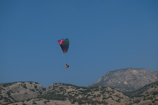 A paraglider gliding through the sky with a colorful sail against a backdrop of a deep blue sky and rocky mountains. Adrenaline and adventure. - Powered by Adobe