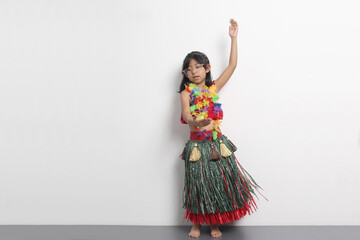 5-year-old Latina girl with brown hair enjoys learning to dance Hawaiian, wearing a colorful skirt and leis, and shows off her moves