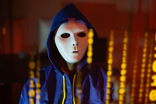 Masked hacker hacking computer. anonymous hacker wearing mask and black hoodie in dark room. online scam and cyber security threat.