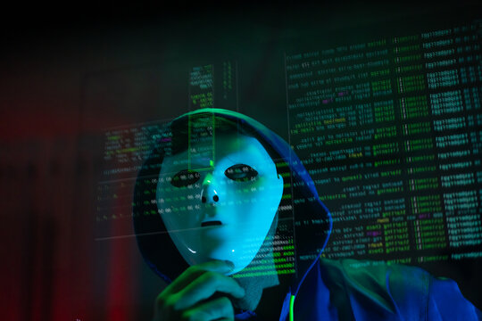 Masked hacker hacking computer. anonymous hacker wearing mask and black hoodie in dark room. online scam and cyber security threat.