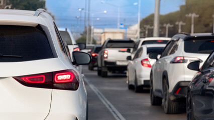 Rear side of car with turn on brake light. Many car driving on the asphalt road. Driving in a queue in traffic jams. Blurred of trees and town with electric pole.