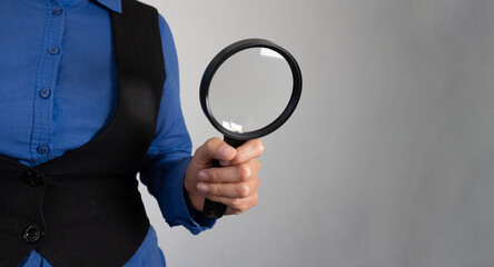 Close-up of a businesswoman's hand holding a magnifying glass against a gradient gray background
