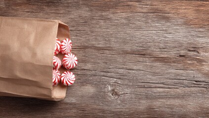 Candy swirls spill from a brown paper bag on a rustic wood surface