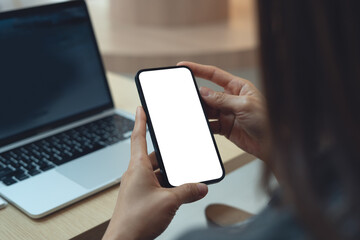 Using smartphone, white screen mockup. Woman using mobile phone with blank white screen during working with laptop on table, cell phone mockup for social media marketing ads