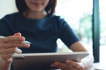 Closeup, woman holding digital tablet and using electronic pen while working at home office. Woman using stylus pen on digital tablet for graphic design work with blurred background