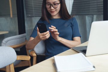 Business casual, digital nomad lifestyle, freelancer at work concept. Business woman sitting at table in coffee shop, using smartphone during remote working on laptop computer at coffee shop