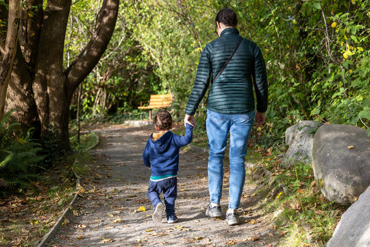 Father And Toddler Walk Handholding Through Park Path, Surrounded By Greenery - Powered by Adobe