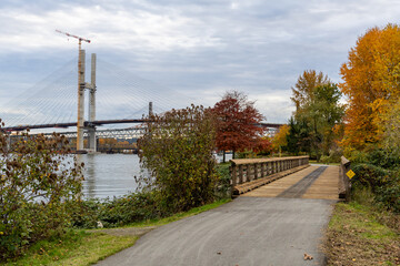 Autumn Riverside Park With Wooden Bridge And Suspension Bridge Over Calm Water In New Westminster
