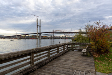 Fototapeta premium Riverfront Walkway With Under-Construction Bridge And Crane Over New Westminster, Greater Vancouver Area