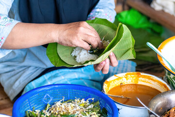 A person is serving Nasi Pecel (traditional Javanese rice salad with peanut sauce) on a teak leaf wrap. Authentic Indonesian street food and culinary concept