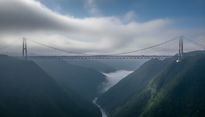 A majestic suspension bridge spans a deep, fog-filled river canyon under a cloudy sky.