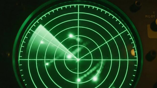 Close-up view of a vintage green radar screen displaying multiple blips and a sweeping radar beam across a dark background with visible dust particles adding a gritty