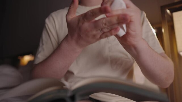 Slow motion closeup of a frustrated man's hands ripping a paper page out of a book, crumpling it into a ball, and throwing it away in a dark, moody room lit by a bedside lamp