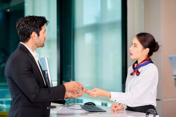 A businessman in black suit show his mobile phone for check in to air ground staff at airport counter check in.