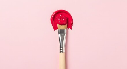 Close up of a paintbrush with vibrant red paint on a soft pink background